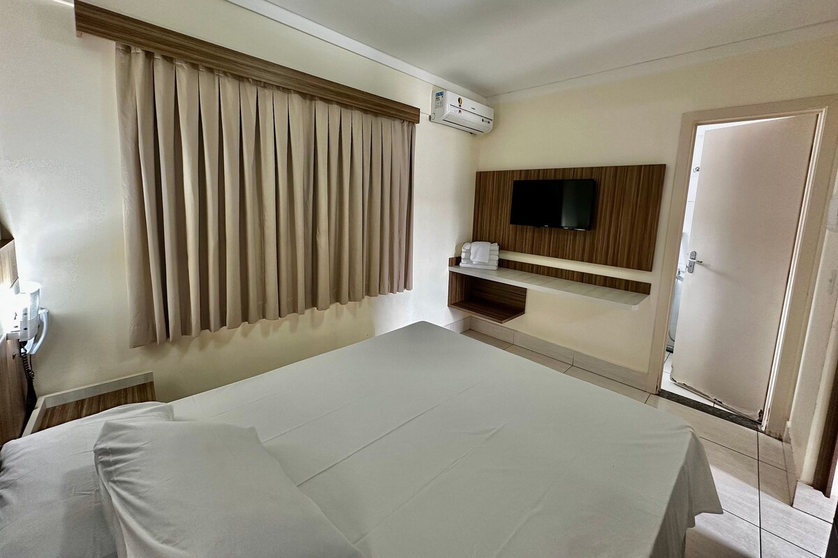 Una habitación de hotel con cama, televisor montado en la pared, armario y aire acondicionado.