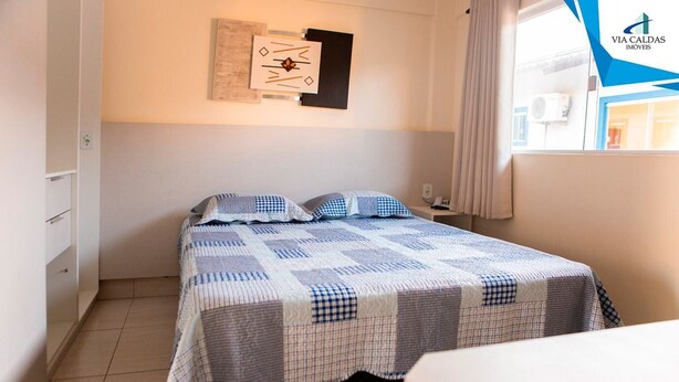 A bedroom with a bed, a nightstand, a wall clock, and a window with curtains. - Lacqua DiRoma V Via Caldas (Caldas Novas)