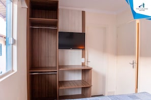 Una habitación con un armario de madera, televisor montado en la pared y una puerta.