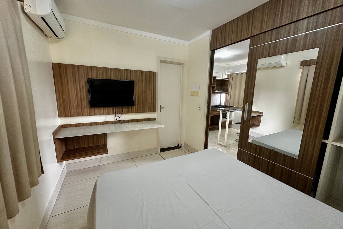 Habitación de hotel con cama, televisor montado en un panel de madera, armario con espejo y equipo de aire acondicionado.