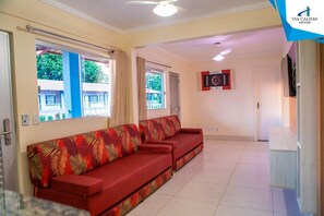 A living room with a red sofa, large windows, a ceiling fan, and a framed picture on the wall. - Lacqua DiRoma V Via Caldas (Caldas Novas)