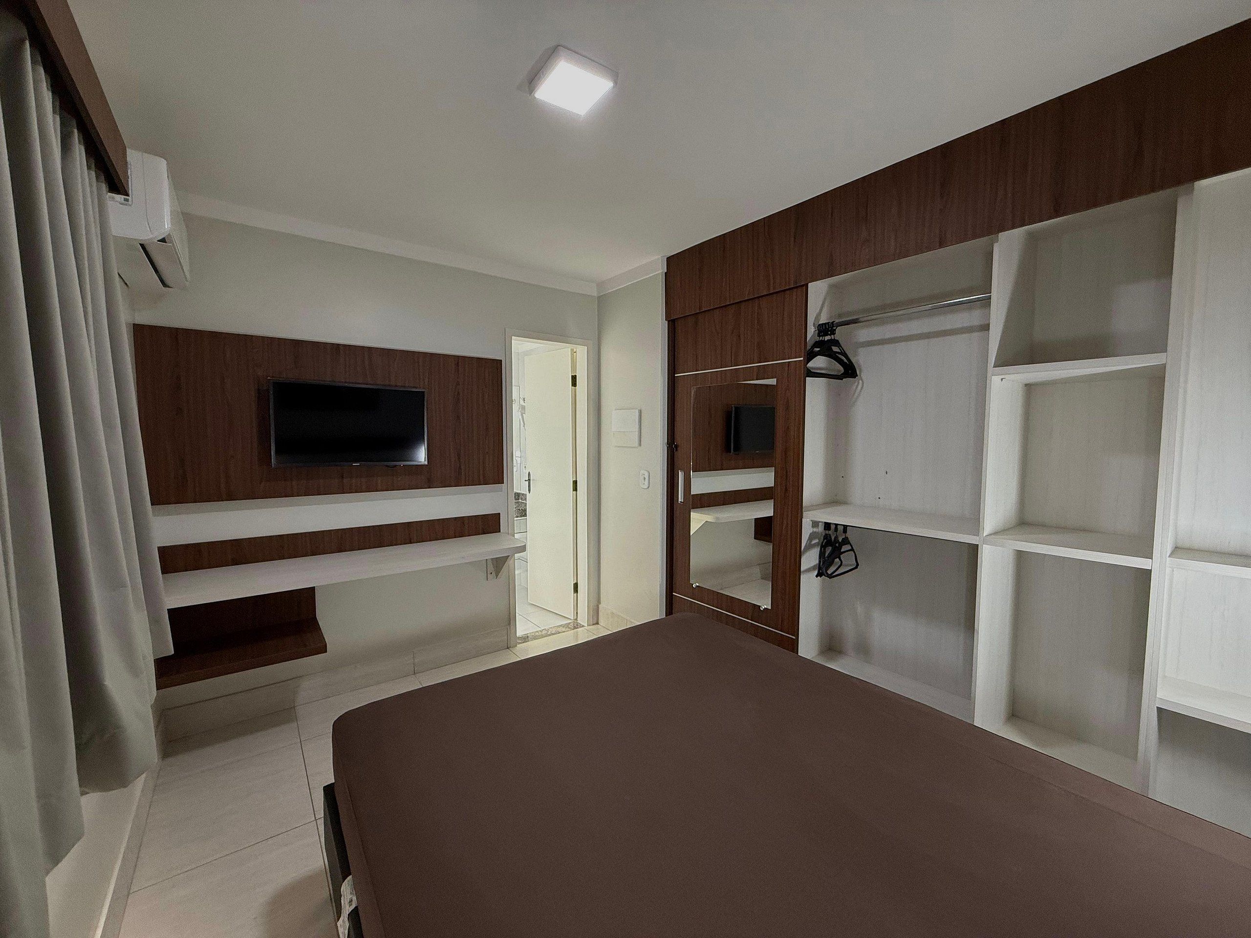 A bedroom with a TV, built-in shelves, a wardrobe, and a bed.