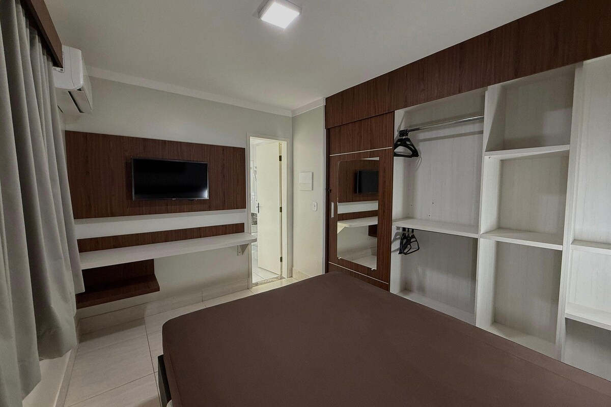 Un dormitorio con televisor, estanterías empotradas, armario y cama.