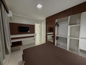 Un dormitorio con televisor, estanterías empotradas, armario y cama.