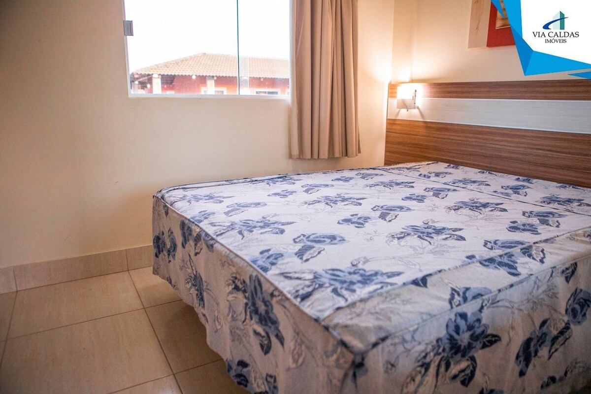 Habitació d'hotel amb llit, finestra amb cortines, làmpada penjada a la paret i un logotip a la paret.