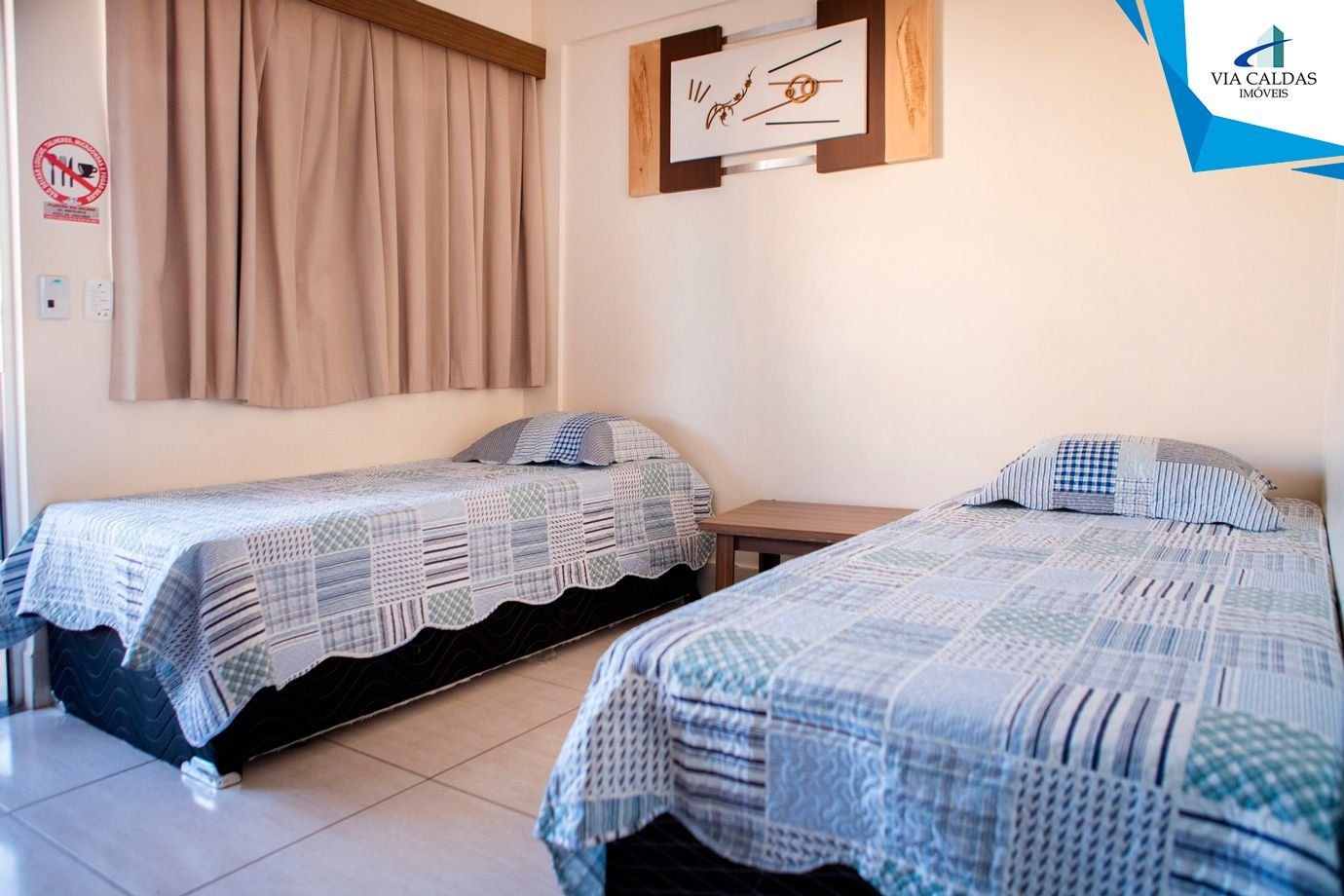 A room with two beds, a wooden nightstand, a wall clock, and a 'No Smoking' sign.