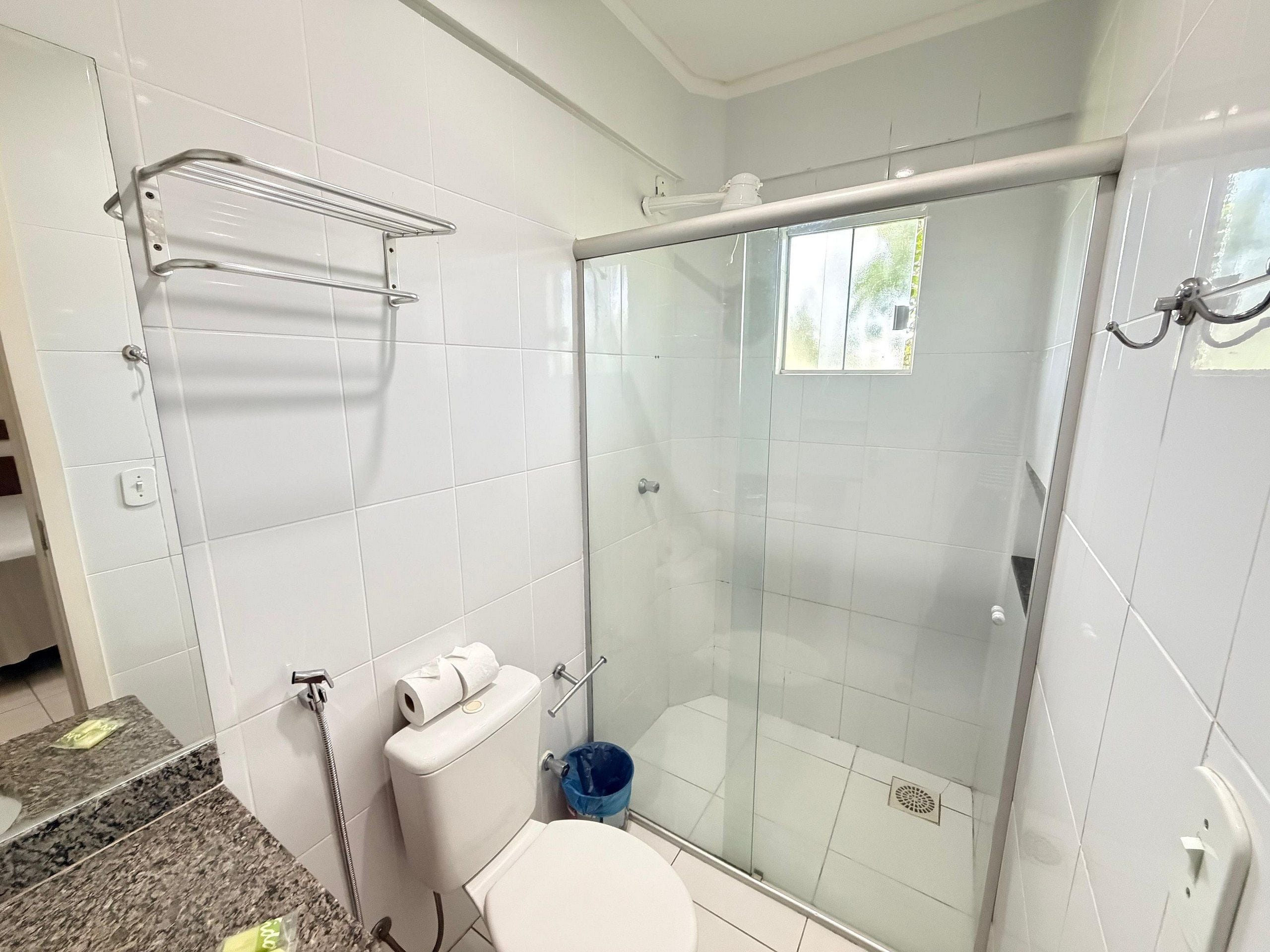 Un baño con ducha de vidrio, inodoro, perchero y encimera de mármol.