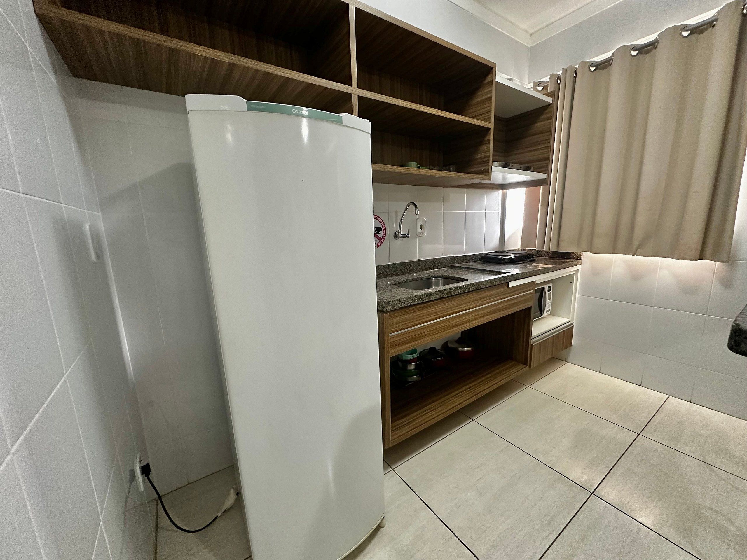 Cocina compacta con refrigerador integrado, un lavabo y estantes de madera.