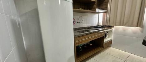 A compact kitchen with a built-in refrigerator, a sink, and wooden shelves.