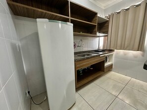 Cocina compacta con refrigerador integrado, un lavabo y estantes de madera.