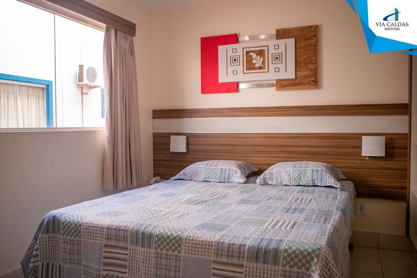 Ett hotellrum med en säng, gardiner, ett fönster och ett konstverk som hänger på väggen.