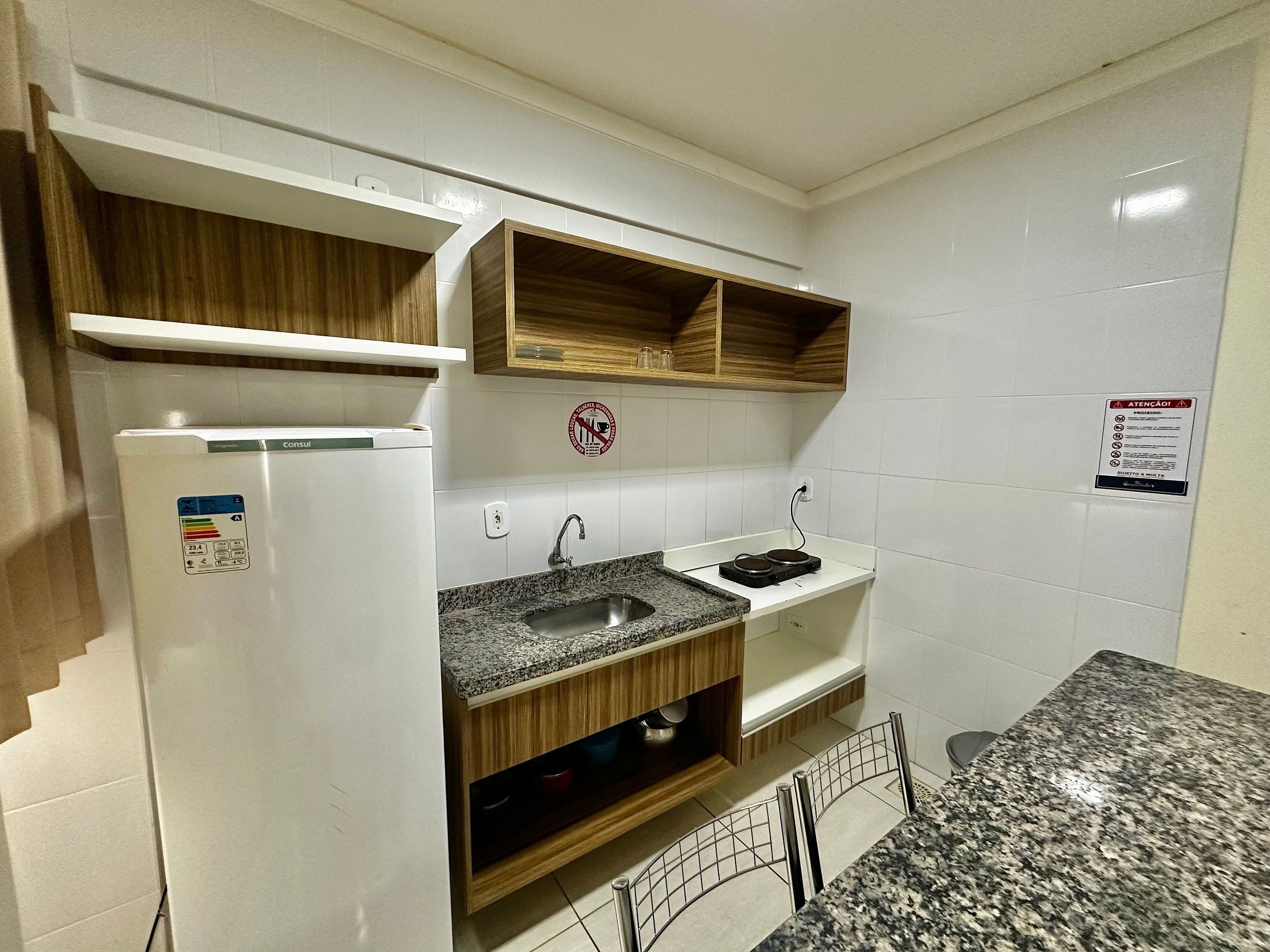 Uma cozinha compacta com geladeira embutida, bancada de granito, armários de madeira e pia de aço inoxidável.