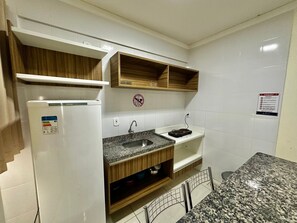 Una cocina compacta con refrigerador integrado, encimera de granito, gabinetes de madera y pileta de acero inoxidable.