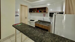 A kitchen with a granite countertop, white cabinets, a microwave, and a refrigerator. - Lacqua DiRoma V Via Caldas (Caldas Novas)