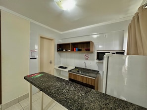 A kitchen with a granite countertop, white cabinets, a microwave, and a refrigerator. - Lacqua DiRoma V Via Caldas (Caldas Novas)