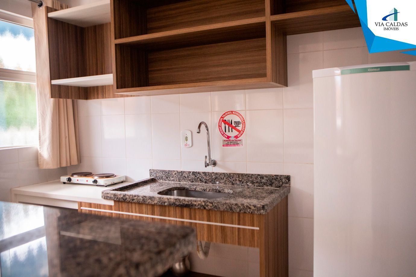 A kitchen with wooden cabinets, a granite countertop, a stainless steel sink, a white refrigerator, and a window with curtains.