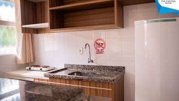 A kitchen with wooden cabinets, a granite countertop, a stainless steel sink, a white refrigerator, and a window with curtains.