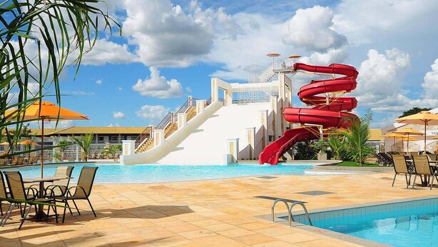 Zona de piscina con tobogán, sillas de descanso y sombrillas.