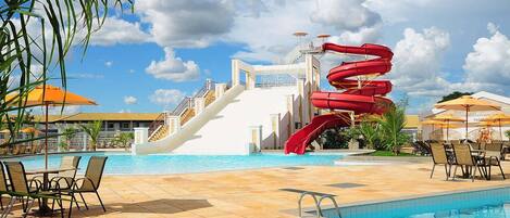 A pool area with a water slide, lounge chairs, and umbrellas.