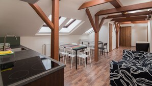 A modern kitchen with a black stove, white chairs, and a dining table with a colorful placemat. - Easy Housing Hostel (Prague)