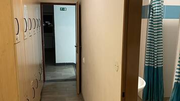 Un pasillo con casilleros, un baño con cortinas a rayas y una señal de salida visible.