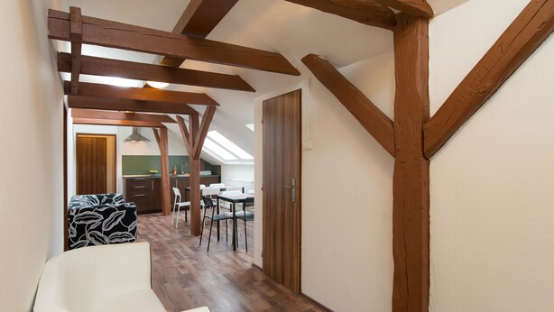 A narrow hallway with wooden beams, a white bathtub, and a dining area with chairs and a table. - Easy Housing Hostel (Prague)