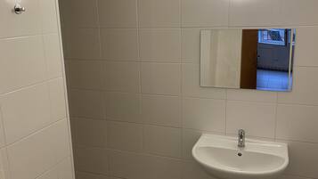Un baño con azulejos blancos, suelo de madera, un lavamanos y un espejo.