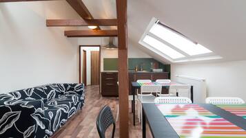 Une pièce chaleureuse avec un lit en mezzanine, une table à manger avec des chaises, un coin cuisine et une lucarne.
