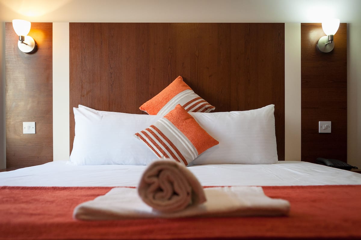 Ein Hotelzimmer mit einem Holzkopfteil, weißer Bettwäsche und zwei Wandleuchten.