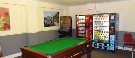 A pool table in a room with vending machines and a ceiling fan.