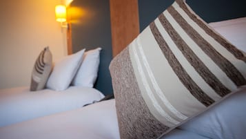 A hotel room with a bed, pillows, and a wall-mounted light fixture.