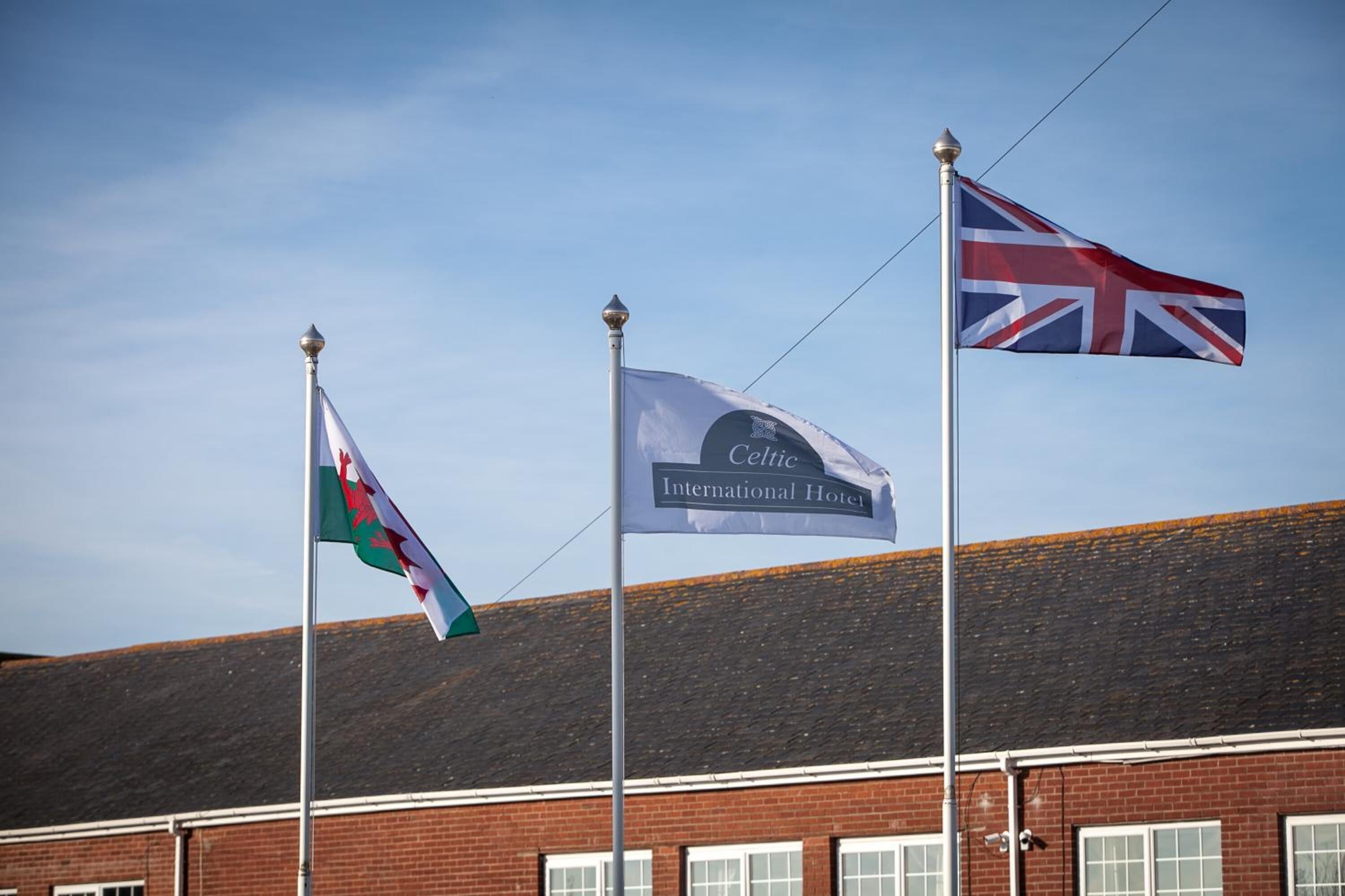 Three flags on flagpoles in front of a building with a red brick facade.