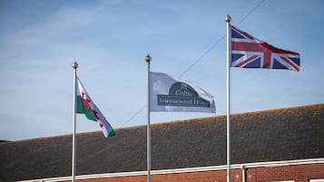 Three flags on flagpoles in front of a building with a red brick facade.