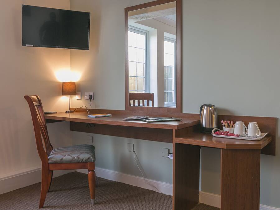A hotel room with a desk, chair, TV, and a tray with cups and a kettle.