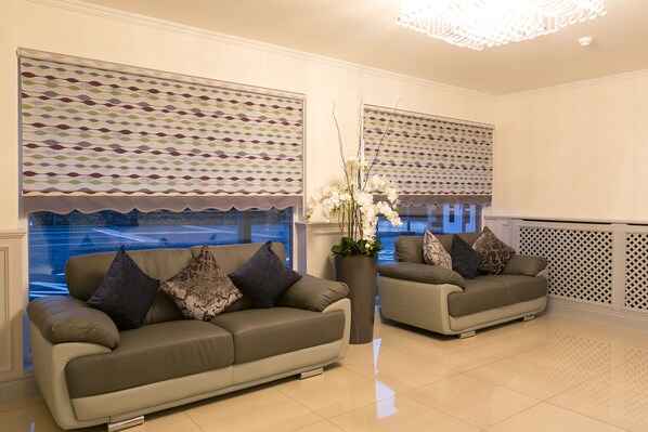 Un salón moderno con dos sofás, un jarrón grande con flores blancas y cortinas con diseño.