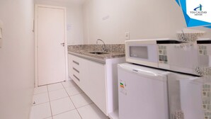Una cocina con armarios blancos, encimera de granito, microondas integrado y refrigerador.