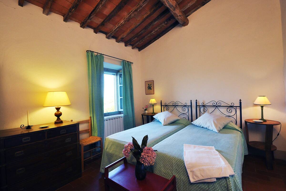 A bedroom with two beds, a dresser, a window with curtains, and two bedside lamps.