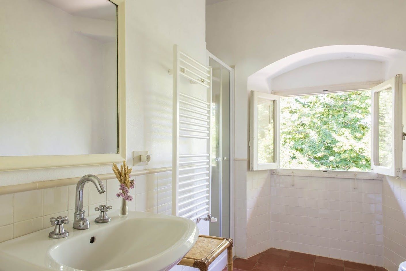 A bathroom with a white sink, mirror, and window with a view of greenery.