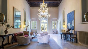 A spacious living room with a chandelier, floral armchairs, a coffee table, and a large painting on the wall. - Petrolo (Bucine)