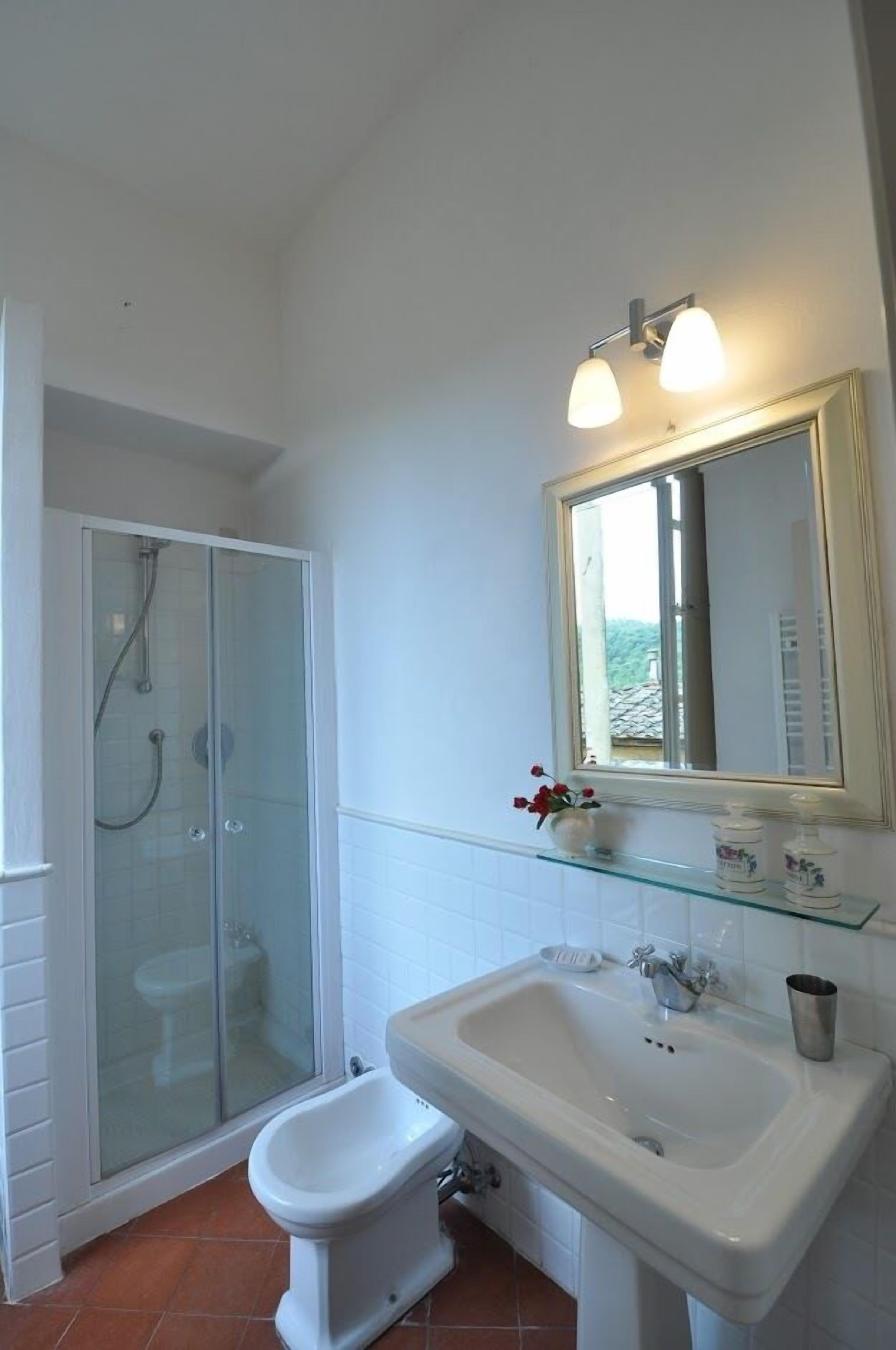 A bathroom with a glass-enclosed shower, a white sink, and a mirror with a light fixture.