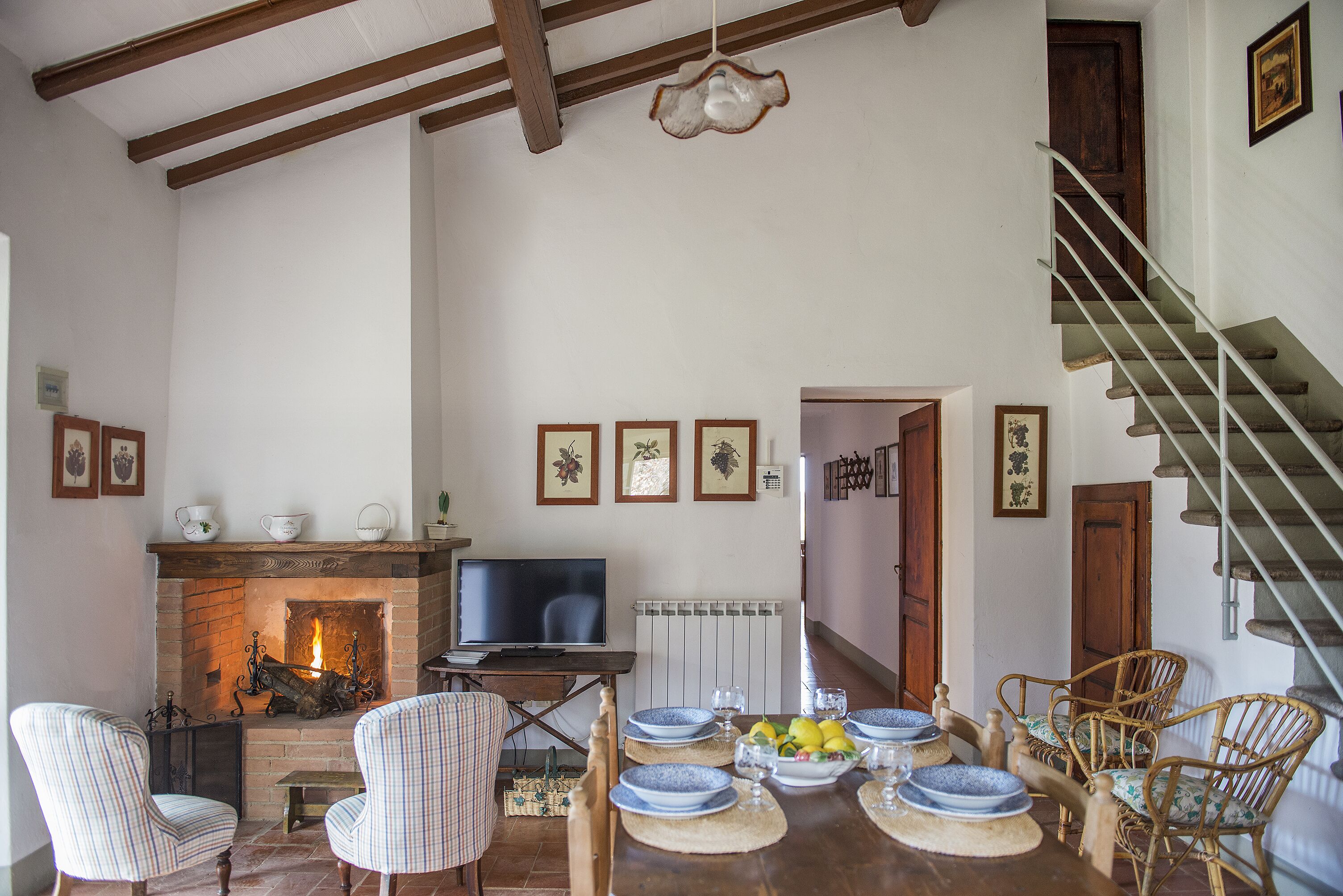 Een gezellige woonkamer met een open haard, een eettafel gedekt met borden en glazen, en een trap die naar een verdieping leidt.