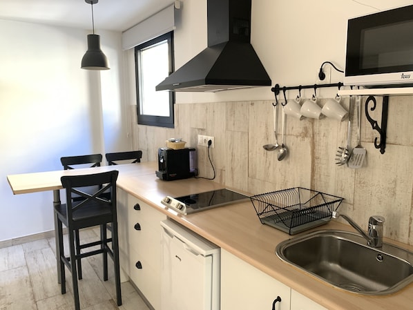 A modern kitchen with a wooden countertop, a black range hood, a microwave, and a sink. - Gorbea Suites (Monachil)