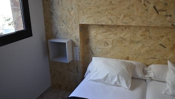 Un dormitorio con cabecera de madera, cama con ropa de cama blanca y una pequeña estantería blanca.