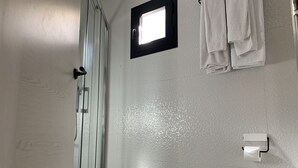 A bathroom with a glass shower enclosure, a white toilet, and a small window. - Gorbea Suites (Monachil)