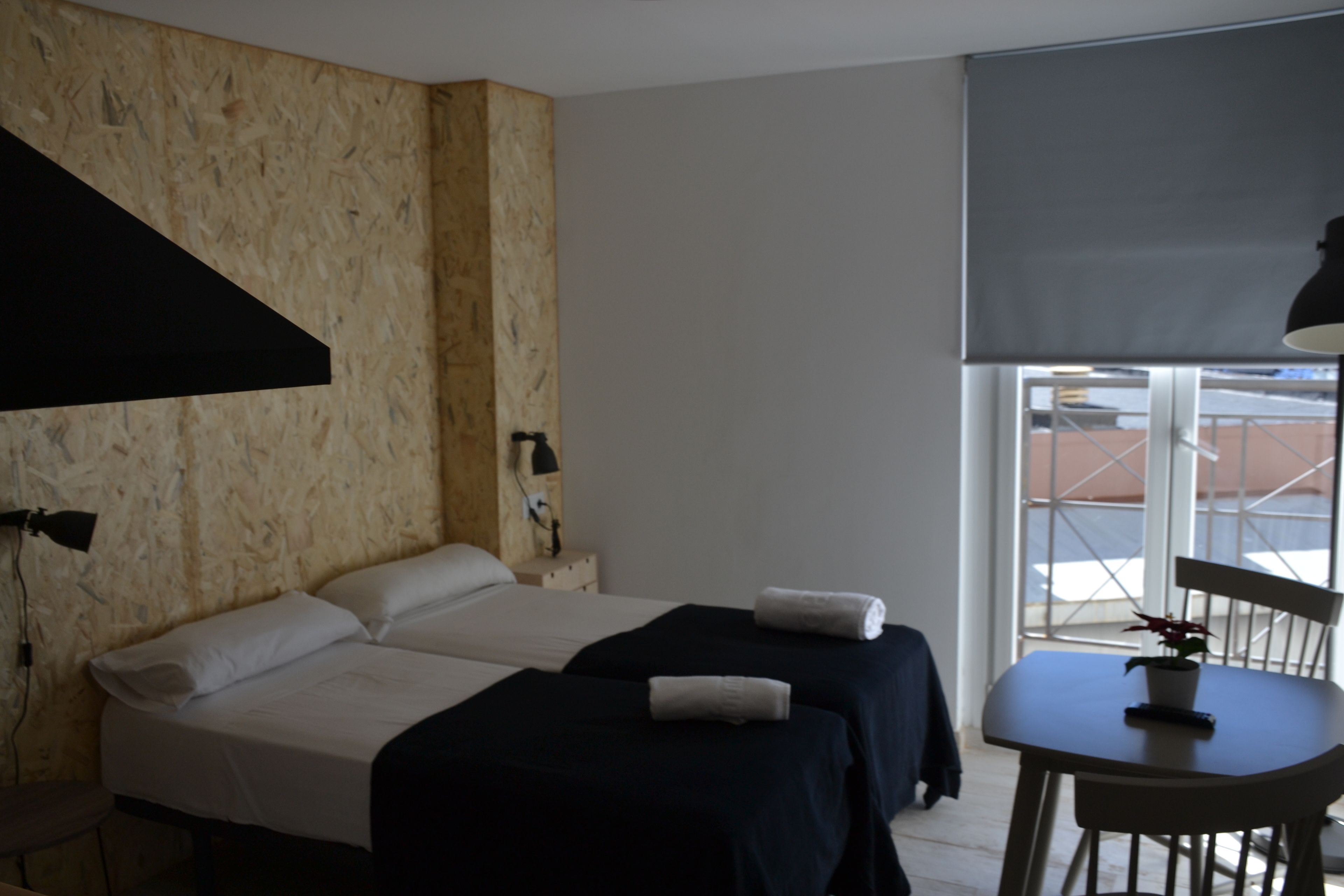 Una habitación con dos camas, una mesita y un ventanal.