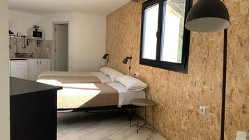 Ein Schlafzimmer mit Bett, Nachttischen, einem Fenster und einer kleinen Küche im Hintergrund.