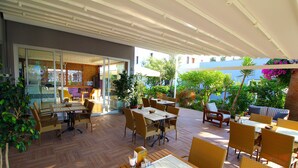 An outdoor patio with wooden tables and chairs, a glass door entrance, and potted plants. - The Losh (Bodrum)