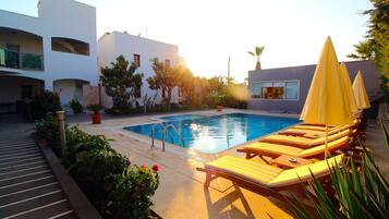 Una piscina al aire libre, sombrillas, sillones reclinables de piscina