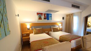 A hotel room with two beds, a wooden headboard, bedside lamps, a painting, and a window with curtains. - The Losh (Bodrum)