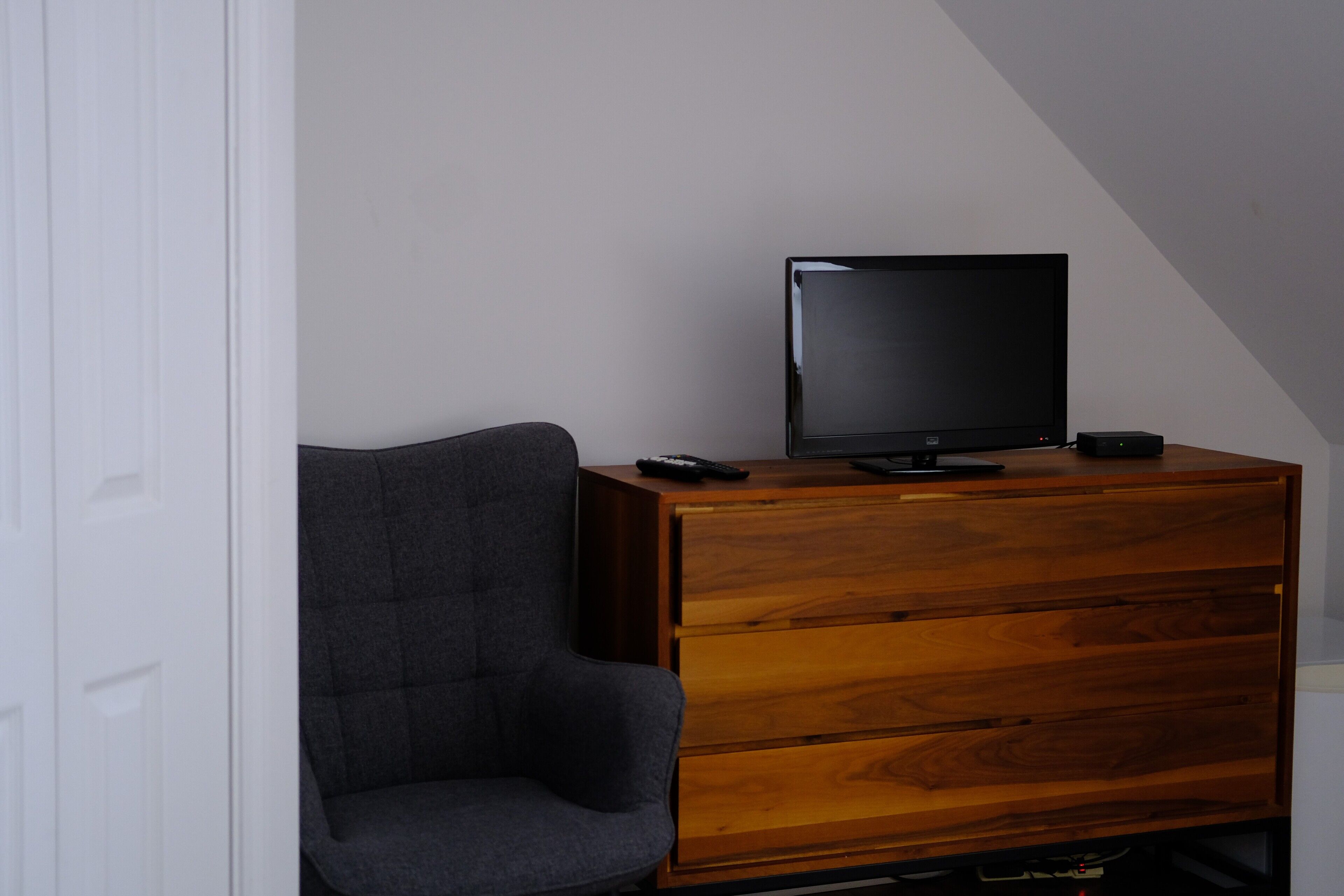A modern room with a wooden dresser, a television on top, and a grey armchair.